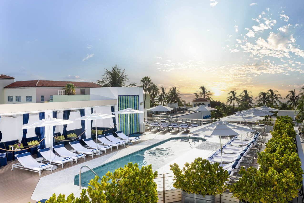 A resort pool with lounge chairs, umbrellas, and palm trees at sunset.