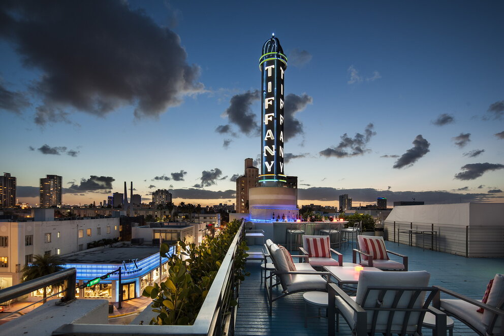 A rooftop bar with seating area overlooking the city skyline at dusk.