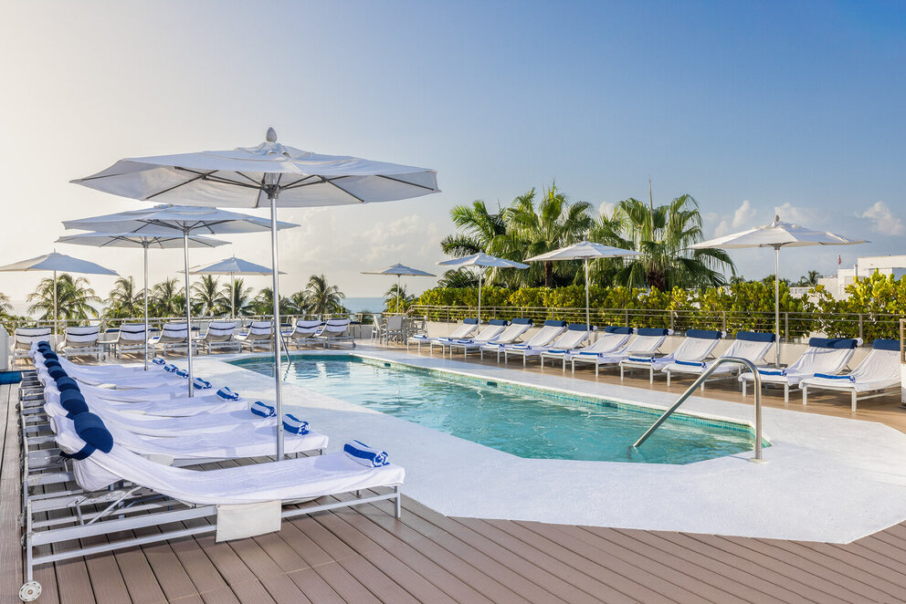 A poolside area with lounge chairs, white umbrellas, and palm trees in the background.